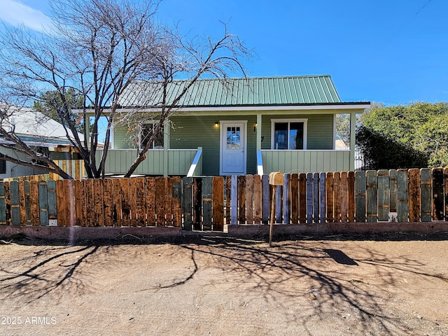 view of front facade with covered porch, a fenced front yard, and metal roof