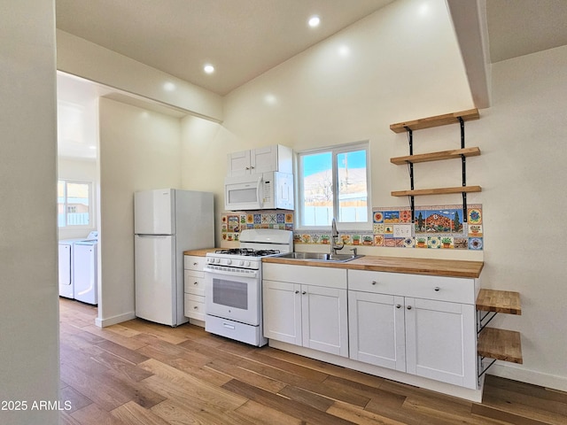 kitchen featuring white appliances, white cabinets, wood finished floors, washing machine and dryer, and a sink