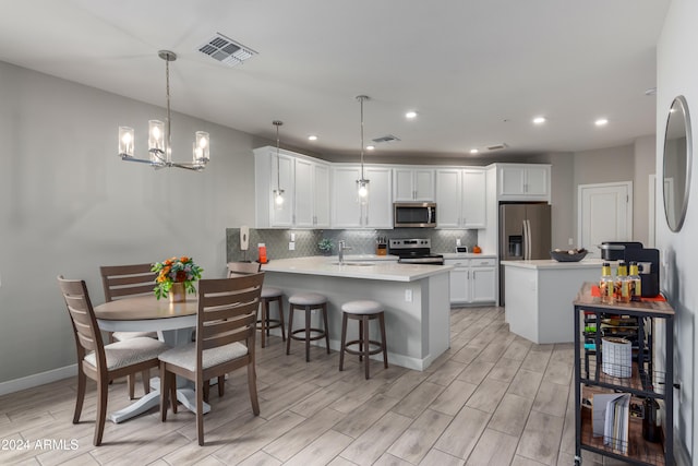 kitchen with stainless steel appliances, kitchen peninsula, decorative light fixtures, white cabinets, and light wood-type flooring