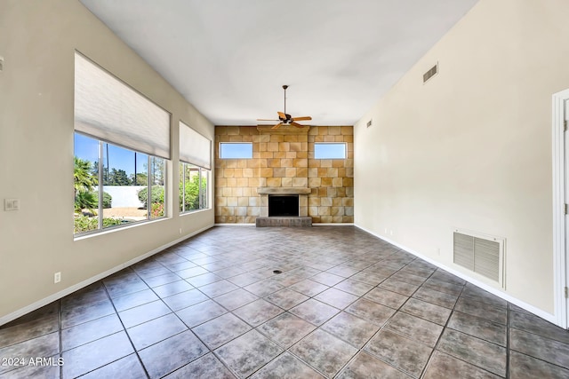 unfurnished living room with a stone fireplace, ceiling fan, and tile patterned flooring