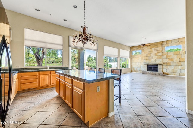 kitchen with a kitchen breakfast bar, a center island, light tile patterned floors, and ceiling fan with notable chandelier