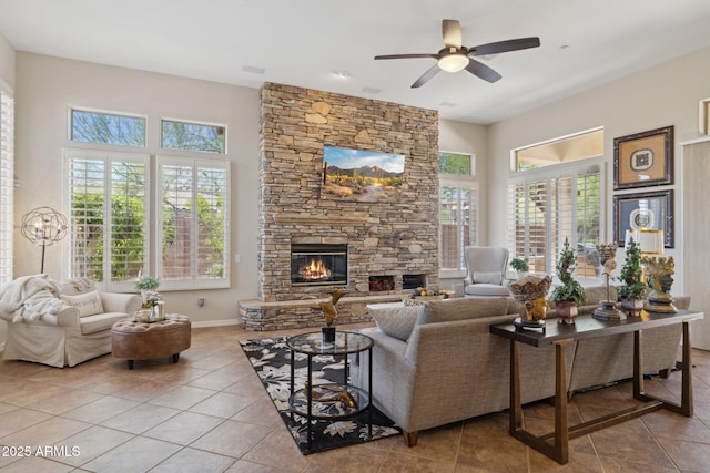 tiled living room with a stone fireplace, ceiling fan, a towering ceiling, and baseboards