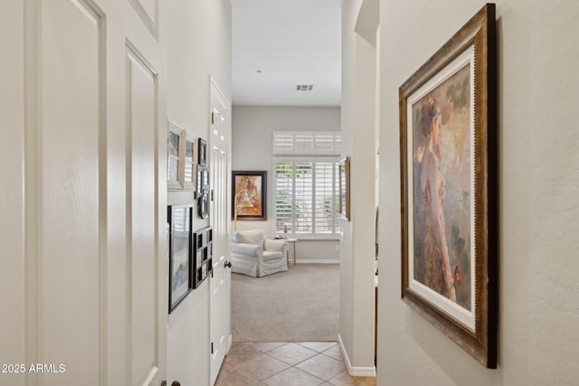 hallway featuring light colored carpet, light tile patterned flooring, and baseboards