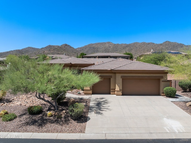 prairie-style home with stucco siding, a mountain view, driveway, a garage, and a tile roof