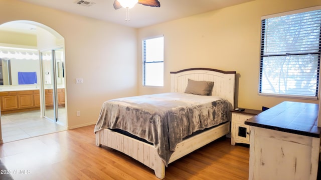 bedroom with light wood-type flooring, visible vents, arched walkways, and connected bathroom