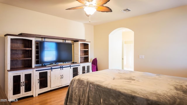 bedroom featuring light wood-style floors, ceiling fan, visible vents, and arched walkways