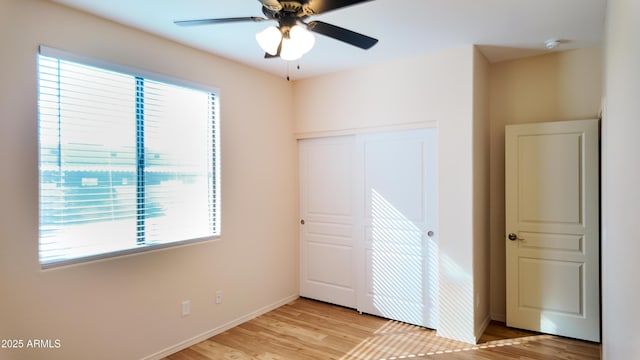 unfurnished bedroom with baseboards, ceiling fan, a closet, and light wood-style floors