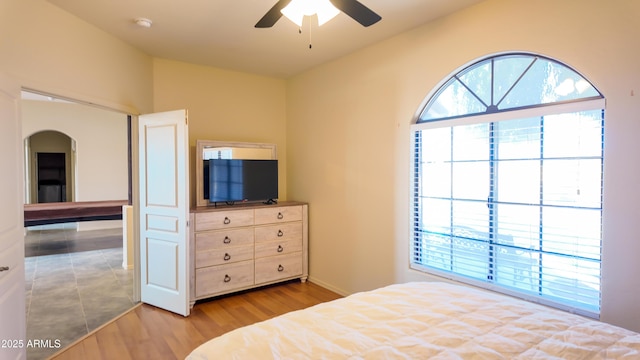 unfurnished bedroom featuring arched walkways, multiple windows, lofted ceiling, and wood finished floors