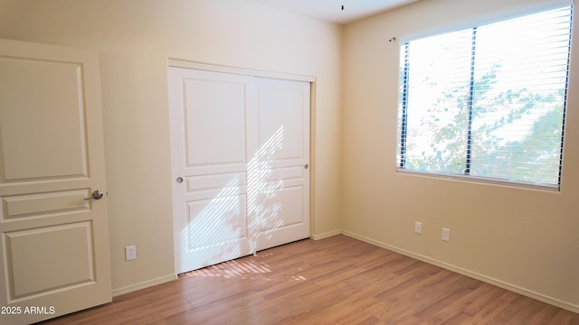 unfurnished bedroom with light wood-type flooring, baseboards, and a closet