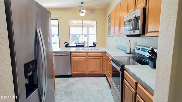 kitchen with stainless steel appliances, light countertops, brown cabinetry, a sink, and ceiling fan