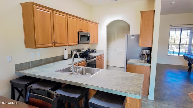 kitchen featuring arched walkways, tile counters, appliances with stainless steel finishes, a kitchen breakfast bar, and a peninsula