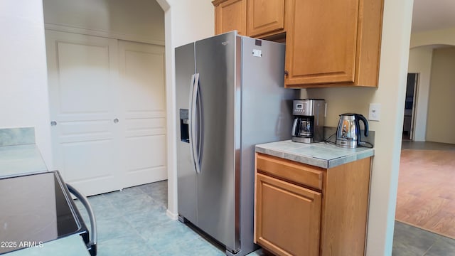 kitchen with range with electric cooktop, brown cabinets, arched walkways, and stainless steel fridge with ice dispenser