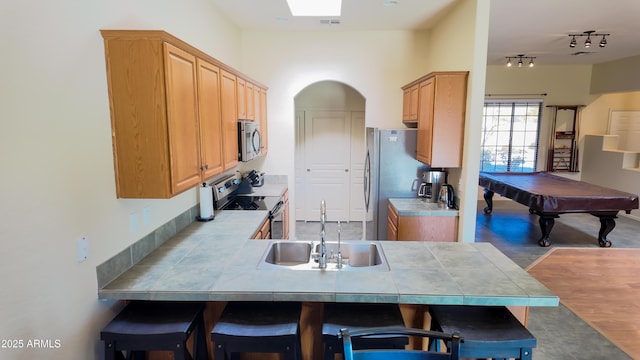 kitchen with tile counters, appliances with stainless steel finishes, a breakfast bar area, a peninsula, and a sink