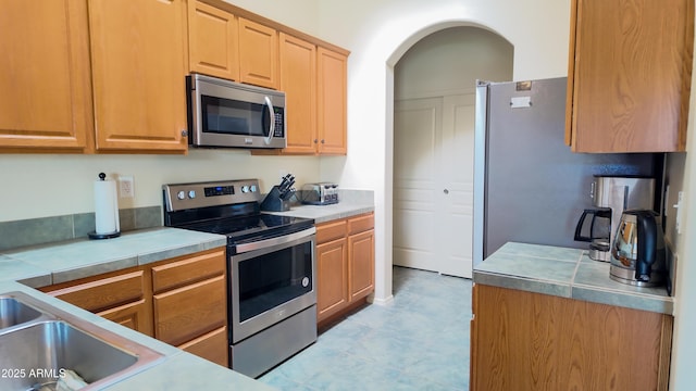 kitchen featuring arched walkways, stainless steel appliances, a sink, and light countertops