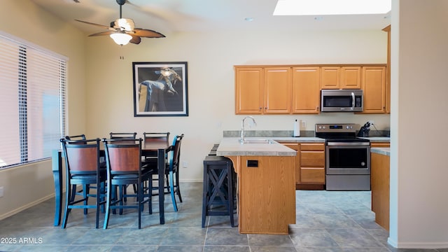 kitchen with a breakfast bar, a sink, baseboards, light countertops, and appliances with stainless steel finishes