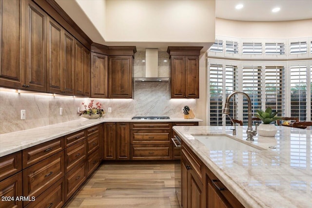 kitchen with wall chimney exhaust hood, light hardwood / wood-style floors, backsplash, and stainless steel gas cooktop