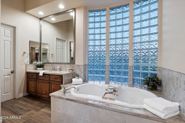 bathroom featuring wood-type flooring, vanity, and tiled tub