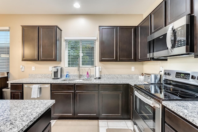 kitchen featuring sink, light tile patterned floors, light stone counters, dark brown cabinetry, and stainless steel appliances