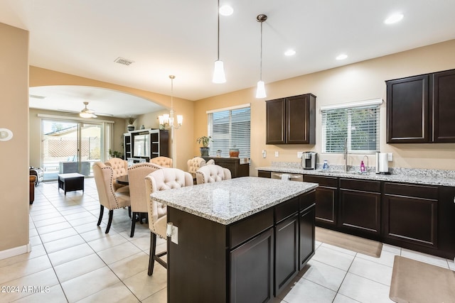 kitchen with dark brown cabinets, ceiling fan with notable chandelier, light tile patterned floors, a center island, and hanging light fixtures