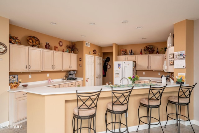 kitchen featuring white refrigerator with ice dispenser, light tile patterned floors, a kitchen breakfast bar, and kitchen peninsula