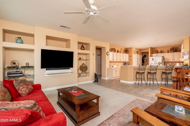 living room with built in shelves, light colored carpet, and ceiling fan