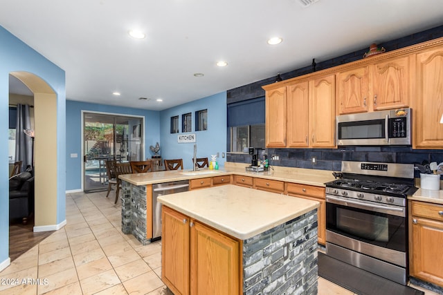 kitchen featuring kitchen peninsula, tasteful backsplash, stainless steel appliances, sink, and a center island