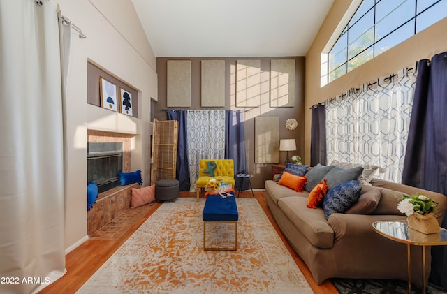 living room featuring light wood-type flooring, a tiled fireplace, and high vaulted ceiling