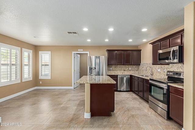 kitchen with a center island, sink, decorative backsplash, appliances with stainless steel finishes, and light stone counters