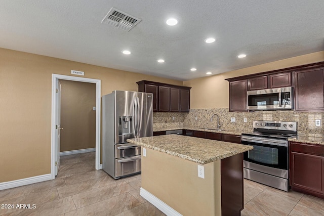 kitchen with sink, stainless steel appliances, tasteful backsplash, a textured ceiling, and a kitchen island