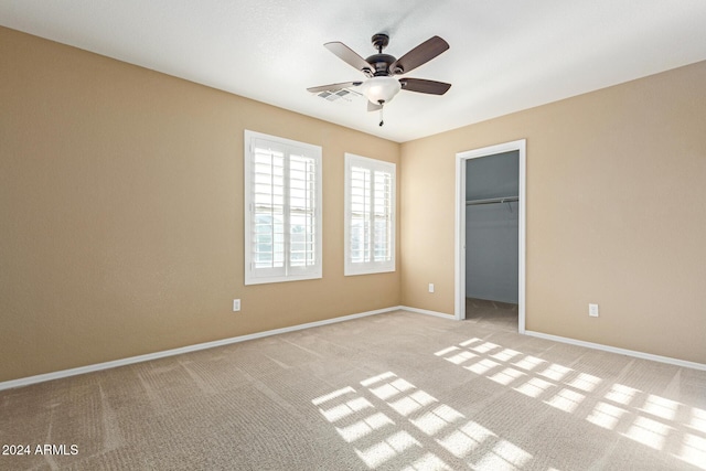 unfurnished bedroom with a spacious closet, a closet, ceiling fan, and light colored carpet