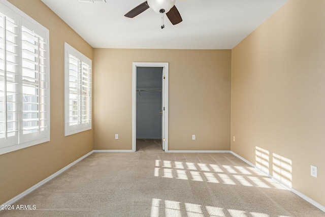 unfurnished bedroom with ceiling fan, light colored carpet, a walk in closet, and a closet