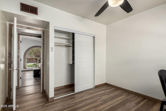 unfurnished bedroom featuring dark wood-type flooring, a ceiling fan, visible vents, baseboards, and a closet