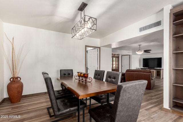 dining room with built in features, baseboards, visible vents, wood finished floors, and ceiling fan with notable chandelier