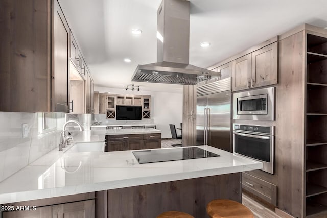 kitchen featuring decorative backsplash, a sink, island range hood, built in appliances, and a peninsula