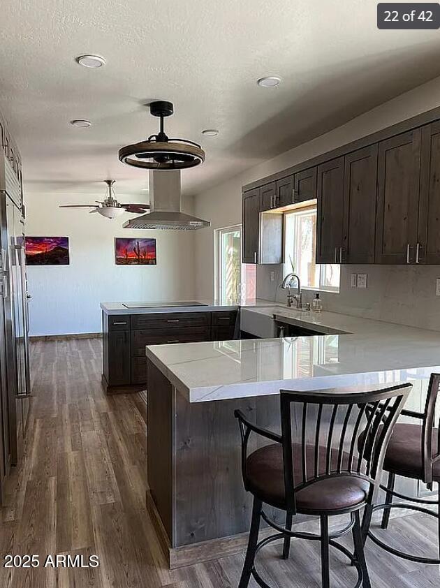 kitchen featuring wall chimney exhaust hood, black electric stovetop, a peninsula, and light countertops