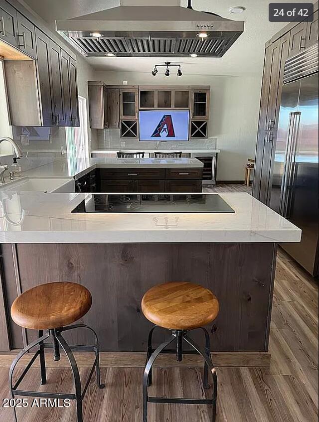 kitchen featuring a sink, stainless steel built in refrigerator, light countertops, wall chimney range hood, and backsplash