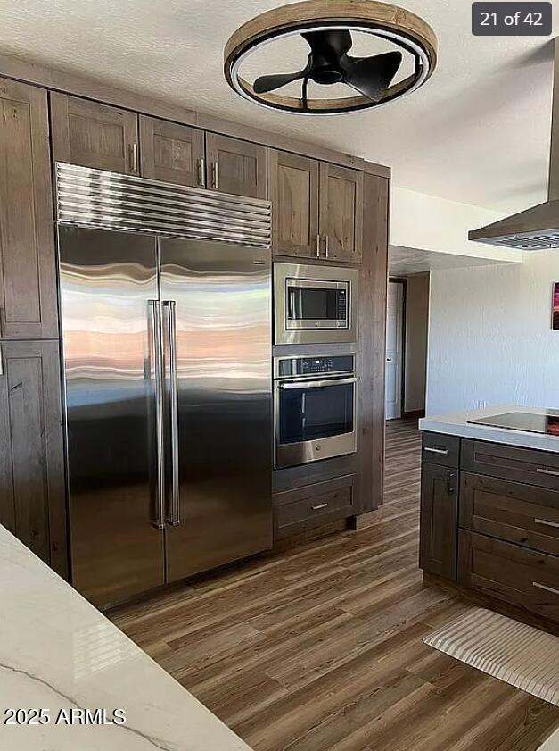 kitchen featuring dark brown cabinets, dark wood finished floors, light countertops, and built in appliances