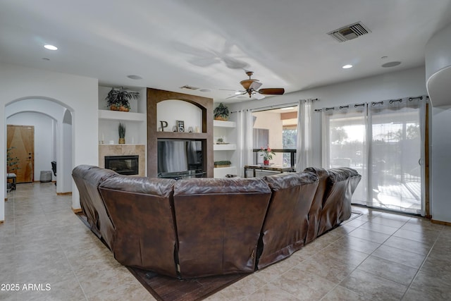 living room with a tiled fireplace, built in features, ceiling fan, and light tile patterned flooring