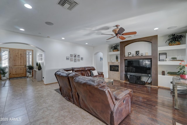 living room with ceiling fan, built in features, a fireplace, and light hardwood / wood-style floors