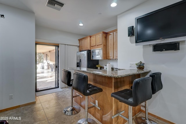 kitchen featuring stainless steel appliances, light tile patterned floors, stone counters, and a kitchen breakfast bar