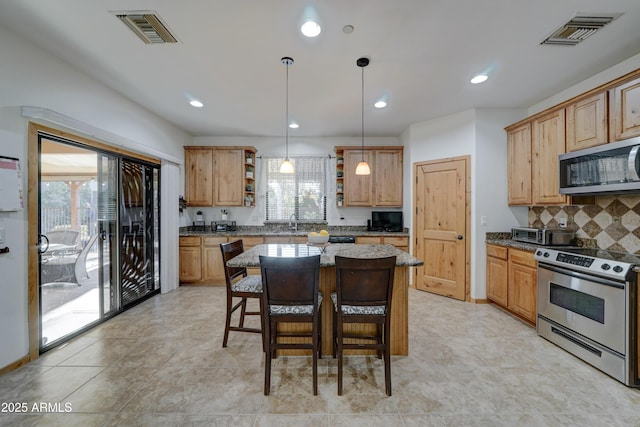 kitchen with pendant lighting, appliances with stainless steel finishes, a center island, light stone counters, and decorative backsplash