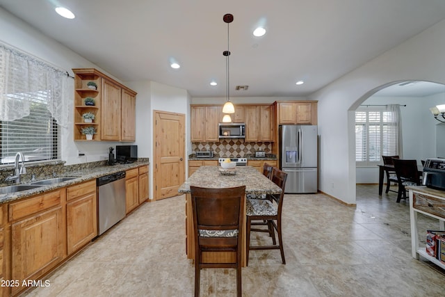 kitchen featuring sink, light stone counters, appliances with stainless steel finishes, a kitchen island, and pendant lighting