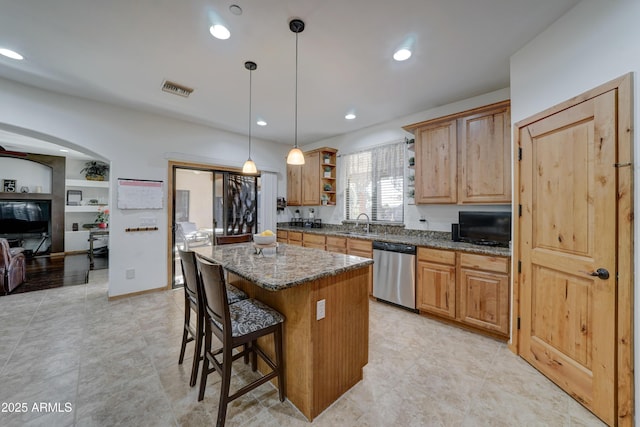 kitchen with decorative light fixtures, stainless steel dishwasher, a center island, and dark stone counters