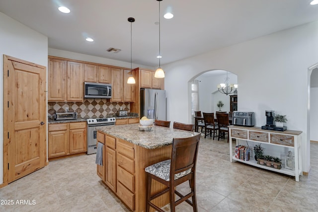 kitchen with pendant lighting, backsplash, stainless steel appliances, a center island, and light stone countertops