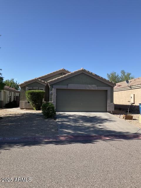 ranch-style home with a tile roof, concrete driveway, a garage, and stucco siding