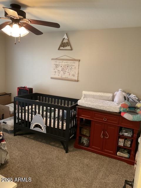 carpeted bedroom featuring a ceiling fan and a nursery area