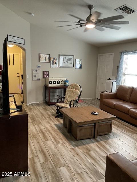 living room with a ceiling fan, lofted ceiling, light wood-style flooring, and arched walkways