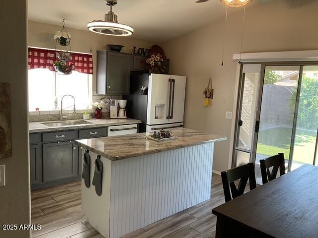 kitchen featuring white appliances, a sink, gray cabinetry, a center island, and light wood finished floors