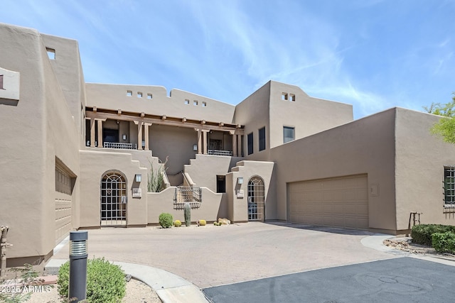 pueblo-style house with an attached garage, driveway, and stucco siding