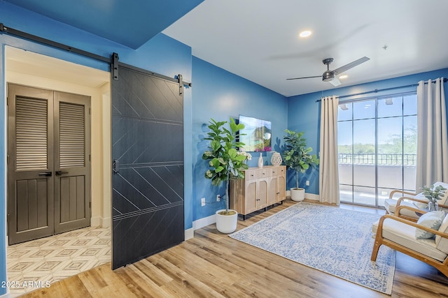 living area featuring a ceiling fan, a barn door, wood finished floors, baseboards, and recessed lighting